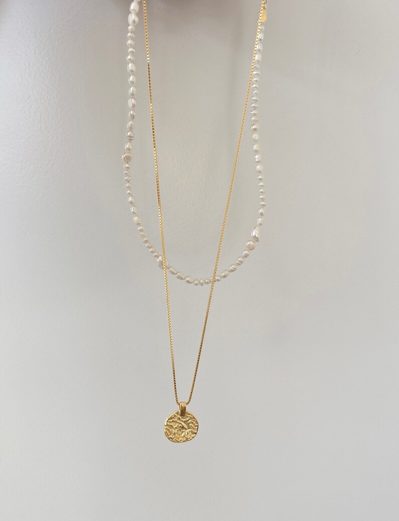 May include: A gold chain necklace with a textured round pendant and a pearl necklace layered on top.