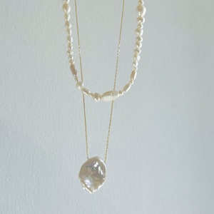 May include: A layered pearl necklace with a large, irregular pearl pendant. The necklace is made of gold chain and features white pearls of varying sizes.