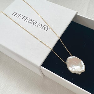 May include: A white baroque pearl pendant necklace on a gold chain in a white box with the text "THE FEBRUARY" on the lid.