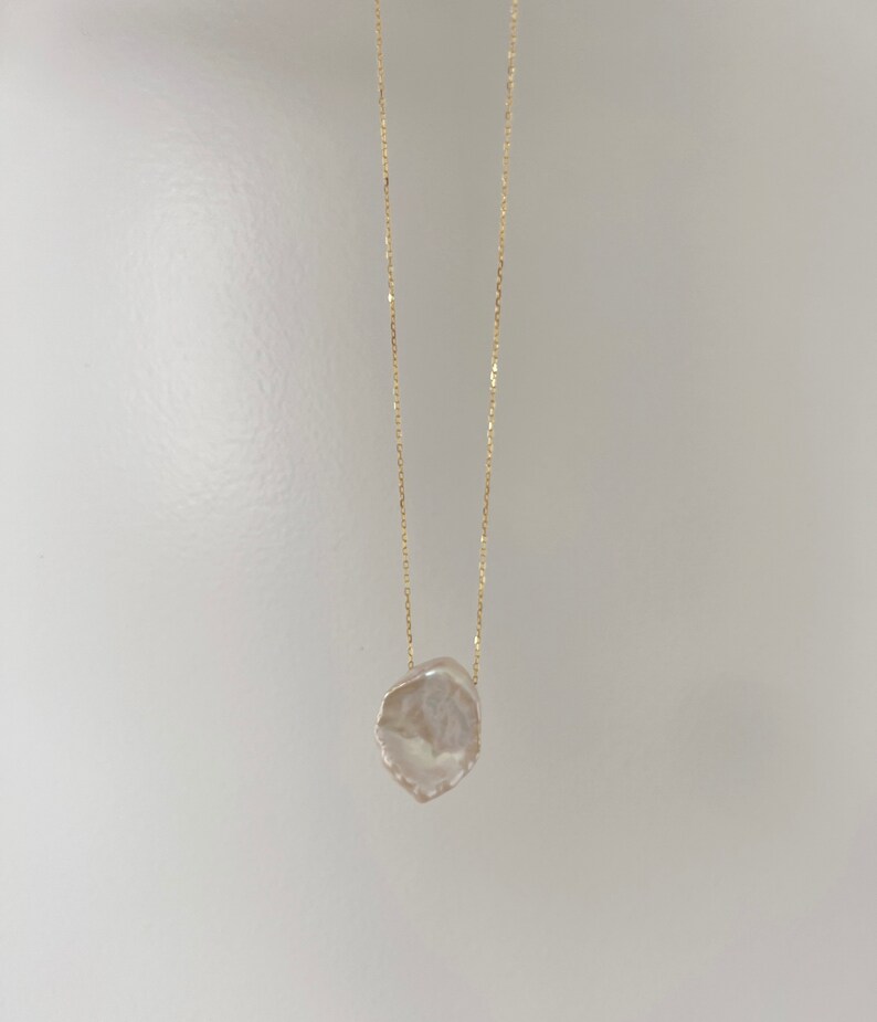 May include: A delicate gold chain necklace with a large, irregular-shaped, white pearl pendant.