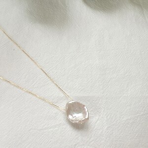 May include: A delicate gold chain necklace with a large, irregular-shaped pearl pendant. The pearl is white and has a slightly iridescent sheen.