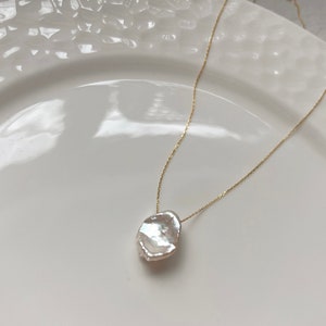 May include: A delicate gold chain necklace with a large, irregular-shaped white pearl pendant.