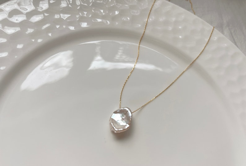 May include: A delicate gold chain necklace with a large, irregular-shaped white pearl pendant.