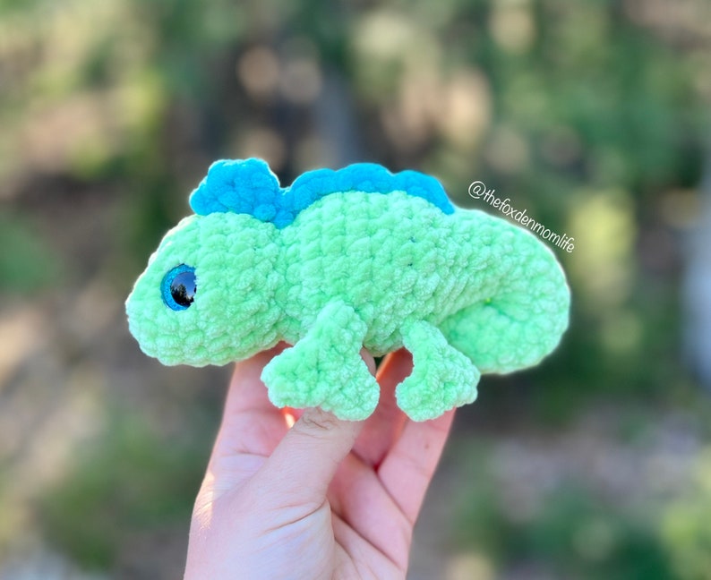 May include: Green crocheted chameleon plush toy with blue accents and large, sparkly eyes.  @thefoxdenmomlife