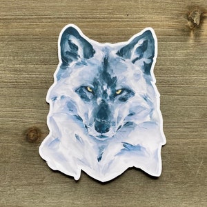 May include: A watercolor painting of a wolf's head with a white and blue color scheme. The wolf has a dark blue nose and yellow eyes.