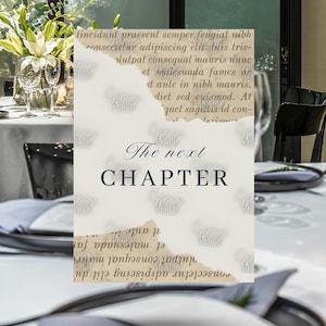 May include: A table setting with a card that reads "The next CHAPTER" in black script. The card has a torn paper design with faded text. The table is set with plates, silverware, and glasses, with a floral arrangement in the background.
