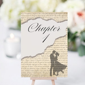 May include: A vintage-style table number card with a distressed paper texture. The card features the text "Chapter 1" in elegant calligraphy and a silhouette of a couple embracing. The card is designed to be displayed on a small easel.