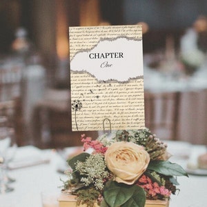 May include: A table number card with a vintage design. The card is made of paper with a distressed look and features a dandelion graphic. The text on the card reads "Chapter One".