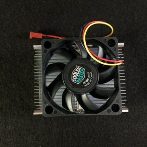 May include: A black computer CPU cooler with a fan and a Cooler Master logo. The fan has a black plastic frame and a silver metal fan blade. The cooler is connected to a black wire with a red and yellow wire.