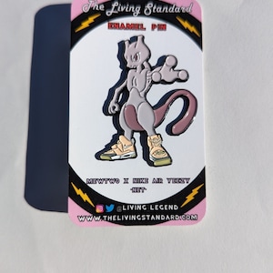 May include: A pink and white enamel pin featuring a cartoon Mewtwo wearing a pair of Nike Air Yeezy sneakers. The pin is on a white card with black text that reads "The Living Standard", "Enamel Pin", "Mewtwo x Nike Air Yeezy", "NET", "@Living Legend", and "www.thelivingstandard.com".