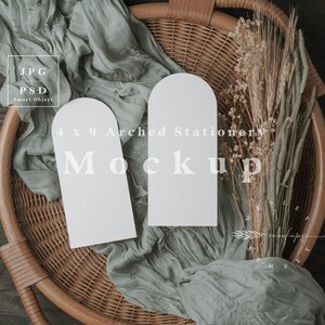 May include: A mockup featuring two 4 x 9 inch arched stationery cards. The cards are white and rest on a woven basket with sage green fabric and dried floral accents. The image includes the text "4 x 9 Arched Stationery Mockup".