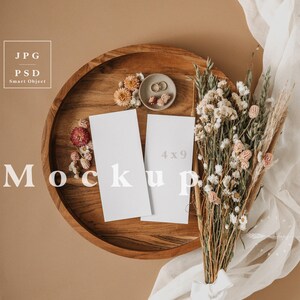 May include: A wooden tray holds two white 4x9 inch mockups, a small dish with rings and flowers, and dried flowers. A bouquet of dried flowers and a white fabric drape across a tan background. The word "Mockup" is displayed.