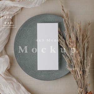 May include: A styled product mockup featuring a gray plate with a white 4x9 menu card. Dried wheat stalks tied with a brown ribbon and a cream-colored fabric drape add texture. The image includes the text "Mockup".