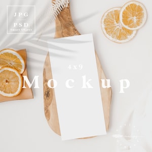 May include: A 4x9 inch white mockup card rests on a wooden cutting board, accompanied by dried orange slices and a small, square, tan-colored tray. The scene is styled with a soft, neutral aesthetic, featuring subtle shadows and a minimalist design.