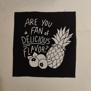 May include: Black and white embroidered patch with the text "Are you a fan of delicious flavor?" and a pineapple and blueberries.
