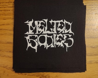 May include: Black square patch with the white text "Melted Bodies" in a gothic font. The patch is stacked on top of other black patches. The patches are likely for clothing or accessories.