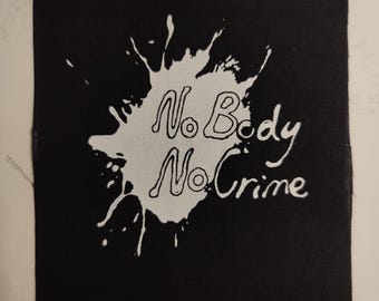May include: Black fabric patch with a white paint splatter design. The text "No Body No Crime" is written in white inside the splatter.