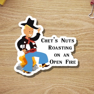 May include: A cartoon cowboy wearing a black vest, blue jeans, and a cowboy hat is standing over a campfire. The text "Chet's Nuts Roasting on an Open Fire" is written in black letters on a white background.