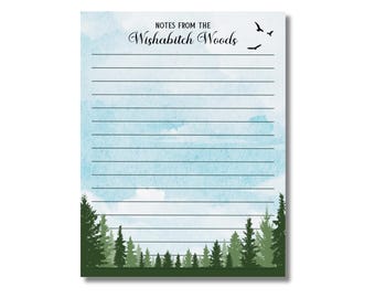 May include: Lined notepad with a watercolor sky and forest design. The notepad features the text "Notes from the Wishabitch Woods" at the top, with silhouettes of birds flying above. The bottom of the notepad has a green forest illustration.