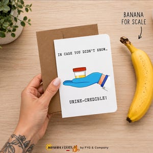 Pu&ograve; includere: Un biglietto d'auguri bianco con busta marrone che presenta l'illustrazione di una mano con guanto medico blu che regge un contenitore per campioni giallo. Il testo recita: IN CASE YOU DIDN'T KNOW... URINE-CREDIBLE! Il biglietto &egrave; accanto a una banana.