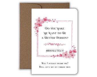 May include: A white greeting card with a brown envelope featuring pink cherry blossom illustrations and a rectangular border. The text reads: Do you make me want to be a better person? Absolutely! Will I actually become one? Well, let's not get carried away.