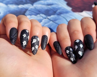 May include: Black almond-shaped nails with a matte finish and white ghost and spiderweb designs.