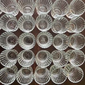 May include: A collection of 25 clear glass ramekins with a fluted design. The ramekins are arranged in five rows of five, with each row offset from the one above it. The ramekins are all empty and appear to be new.