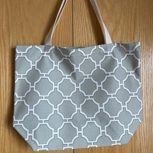 May include: A gray tote bag with white geometric pattern. The bag has two white canvas straps.