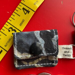 May include: A small black and white fabric coin purse with a black button closure. The purse has a white tag attached that says "Threads and Twists".
