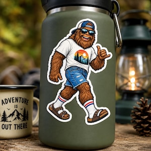 May include: A sticker on a matte olive green water bottle featuring a brown, furry creature wearing a blue baseball cap, dark sunglasses, a white t-shirt with a mountain sunset graphic, blue denim shorts, white socks, and brown sandals.