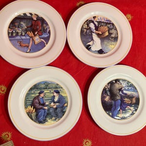 May include: A set of four decorative plates featuring scenes of people in a market and park. Each plate has a white border with a gold trim. The scenes depict people with flowers, bread, and interacting in a park setting.