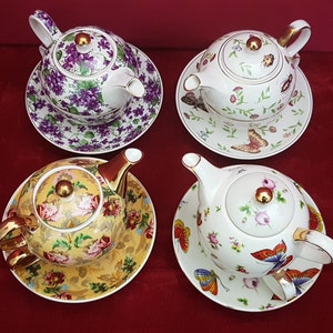 May include: Four teacups and saucers with floral and butterfly designs. Each teacup has a matching saucer with a floral pattern. The teacups are white with gold accents.