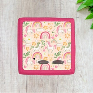 May include: A pink gaming console with a colorful unicorn, rainbow, and star pattern. The console has two black buttons.