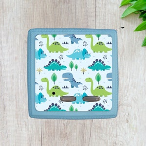 May include: A light blue zippered pouch with a white background and a repeating pattern of green and blue dinosaurs. The pouch has two brown buttons.