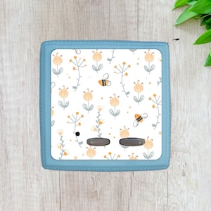 May include: A blue zippered pouch with a white background and a pattern of yellow flowers and bees. The pouch has two black buttons.