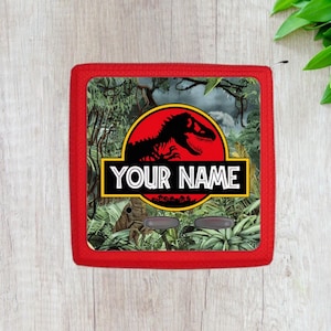 May include: Red and black Jurassic Park logo with a dinosaur silhouette and the text "YOUR NAME" on a red background with a jungle scene.