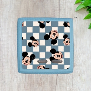 May include: A blue and white checkered fabric storage box with a Mickey Mouse pattern. The box has two black buttons on the front.