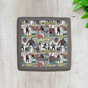 May include: A gray and black wall outlet cover with a repeating pattern of comic book panels featuring Spider-Man. The panels are in black, white, red, and blue. The text "Amazing Spider-Man" appears in several panels.