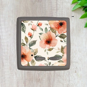 May include: A light switch cover with a floral design featuring watercolor-style pink and peach flowers on a white background.
