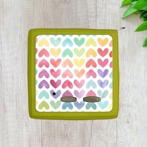 May include: A green zippered pouch with a white background and a pattern of rainbow watercolor hearts. The pouch has two black buttons.