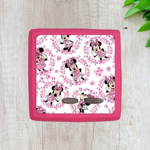 May include: A pink and white square cushion with a pattern of Minnie Mouse characters and pink flowers. The cushion has two gray buttons on the front.