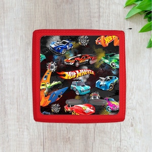 May include: Red rectangular cushion with a black background featuring a repeated pattern of colorful Hot Wheels cars and the Hot Wheels logo.