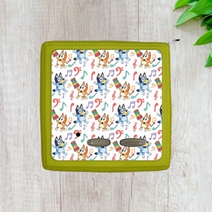 May include: A green zippered pouch with a white background featuring a repeating pattern of blue and orange cartoon dogs playing musical instruments and musical notes.