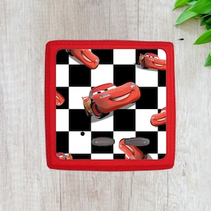 May include: Red square cushion with a checkered pattern and a repeated image of a red race car. The car is on a black and white checkered background.