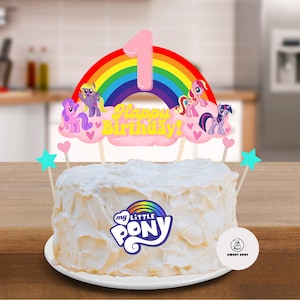 Puede incluir: Un pastel blanco con un logotipo de My Little Pony y un adorno de pastel con temática de arcoíris y unicornio que dice "¡Feliz cumpleaños!"