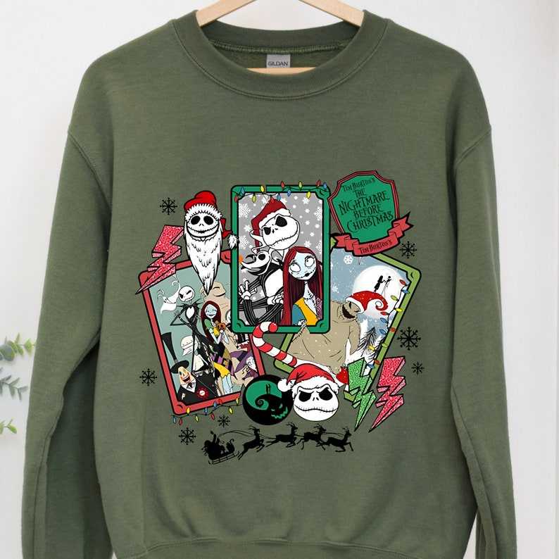 May include: Olive green sweatshirt featuring a graphic design from "The Nightmare Before Christmas." The design includes characters like Jack Skellington, Sally, and others in festive holiday frames, with snowflakes and lightning bolts.