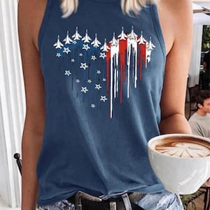 May include: A navy blue vest top with a patriotic design. The graphic features white jets, red and white stripes, and white stars, arranged in a heart shape. The top is worn with blue jeans and a black belt.