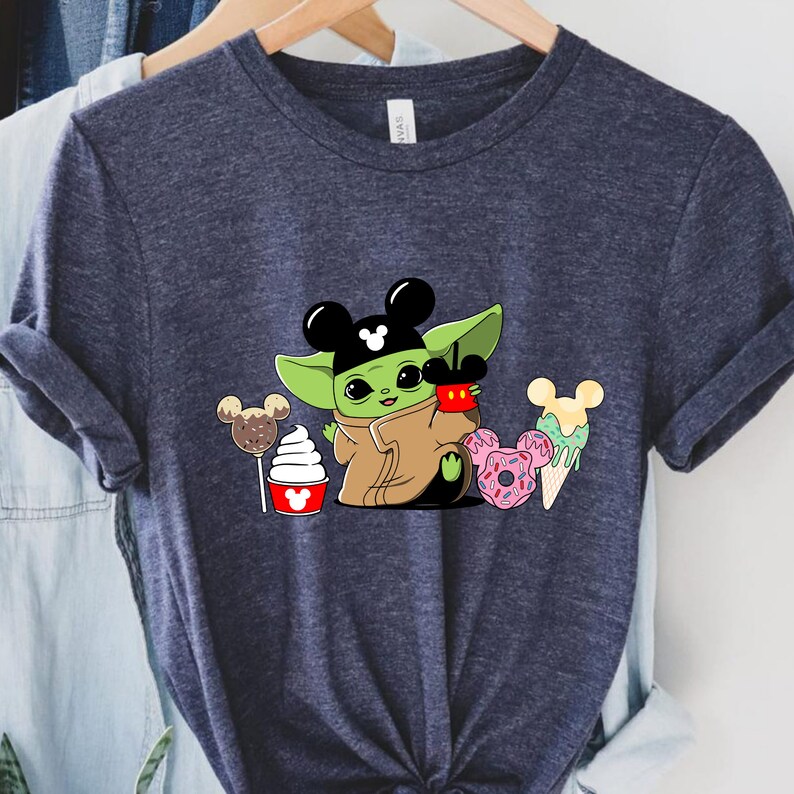 May include: A navy blue t-shirt featuring a cartoon character with green skin and large eyes, wearing a Mickey Mouse hat. The character is holding a red cup with a Mickey Mouse design. Various desserts with Mickey Mouse ears are also shown.