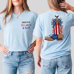 May include: Light blue t-shirts with patriotic designs. One shirt has the text "Brought to you courtesy of the Red, White & Blue." The other shirt shows a cowboy boot with the American flag design and the text "We'll put a boot in your ass. It's the American way."