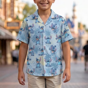 May include: A light blue button-down shirt featuring a repeating pattern of the character Stitch from Lilo & Stitch, with tropical leaves. The shirt has short sleeves and a relaxed fit. The Wondermento Shop logo is visible in the top left corner.